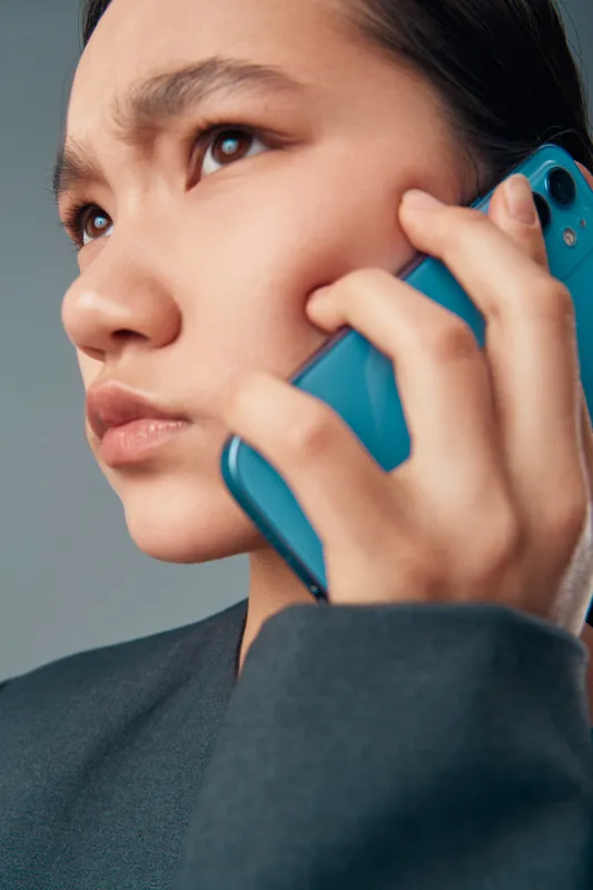 Young woman with serious expression holding blue smartphone to ear for communication conversation or call closeup portrait with focus on face and hand in natural light.
