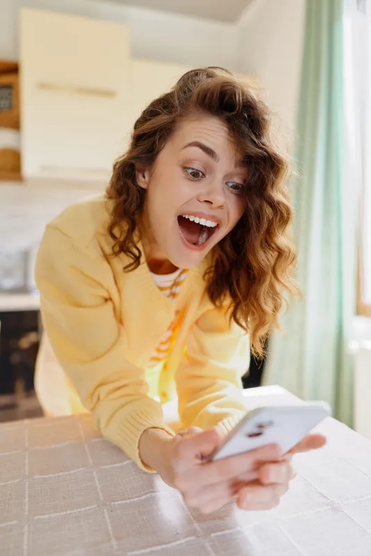 Cheerful woman at home takes a selfie with a phone on a table, bright natural light, casual lifestyle moment, cozy interior, relaxed mood and everyday wellness