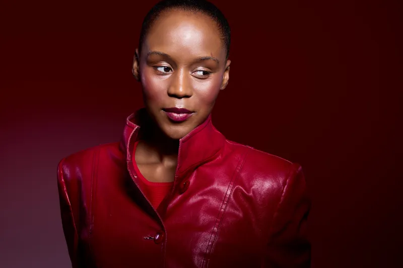 Portrait of a confident dark skinned African American woman wearing a red leather jacket against a red background. The image conveys style, fashion, and empowerment.