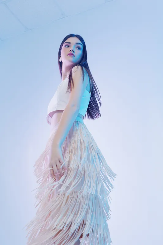 Young woman poses in a stylish fringe skirt and sleeveless top against a light background. Concept for woman beauty fashion, elegance, and modern style.