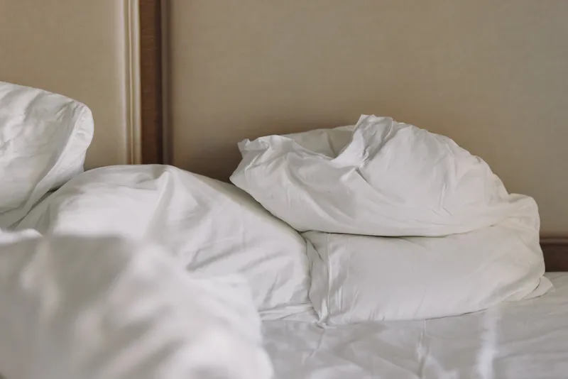 Messy bed with pillows and rumpled sheets in a cozy bedroom, suggesting rest, fatigue and a morning routine after sleep, with soft lighting and calm atmosphere, and cluttered comfort