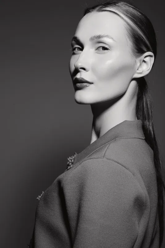 Elegant white woman with fair skin poses confidently in a textured jacket. Black and white studio portrait highlights facial features and sophisticated mood.