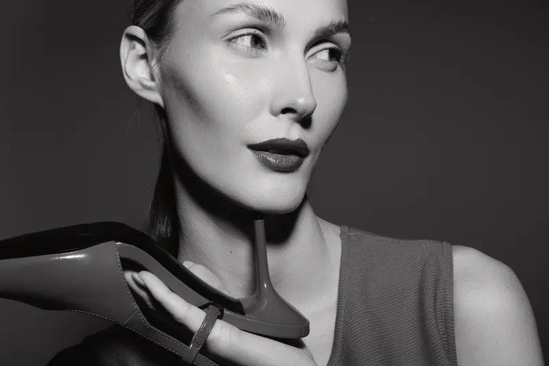Closeup of a young white woman holding a high heel shoe near her face. Black and white portrait with soft lighting, concept for fashion, style, and elegance.
