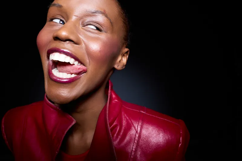 Close-up of a happy black woman with dark skin wearing a red leather jacket smiling and looking to the side. Studio portrait with dramatic lighting and joyful mood concept.