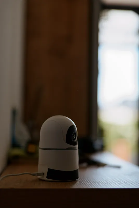 A compact security camera sits on a wooden desk by a bright window, creating a calm home scene. A quiet, modern lifestyle moment focused on privacy and technology.