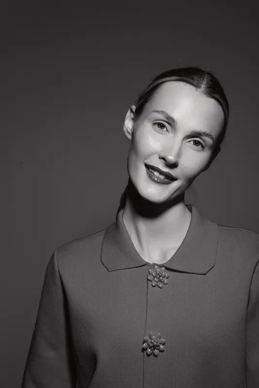 Black and white portrait of a smiling Caucasian woman with fair skin wearing a textured collar dress. Studio lighting highlights her natural beauty and elegant facial expression.