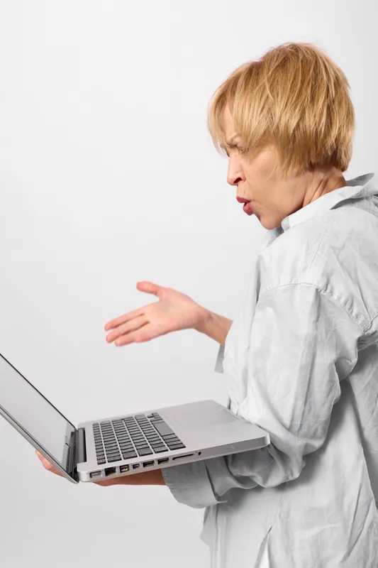 Woman surprised at laptop, computer screen, raises hands in alarmed gesture, focused communication with technology on clean white background, studio portrait closeup.
