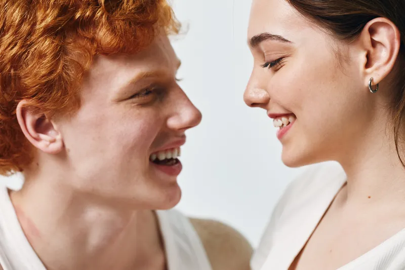 Young man and woman facing each other smiling closely with happy expressions for friendship and connection on white background.