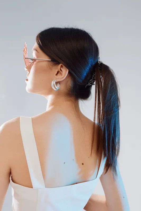 Young woman with long dark hair in a white top and sunglasses looks to the side. Studio shot with soft lighting. Concept for beauty, fashion, and modern style.