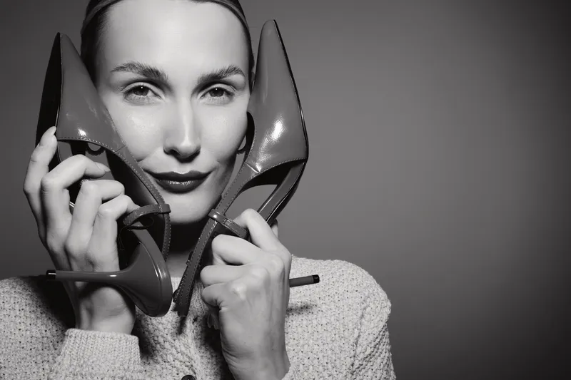 Portrait of a white woman holding high heel shoes near her face. Concept of fashion, beauty, and lifestyle in monochrome studio.