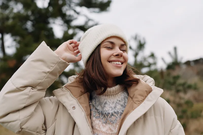Happy woman in a warm beanie and oversized coat enjoying outdoor scenery, candid portrait in natural light, cozy fashion look for chilly weather and relaxed mood today