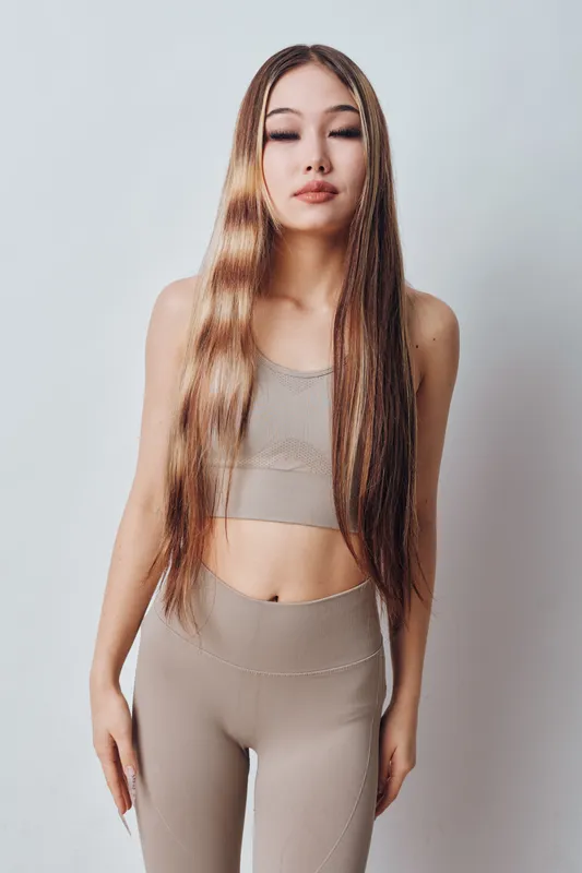 Young woman with long straight hair and braids wearing beige athletic outfit posing with closed eyes on white background for fashion and beauty concept.