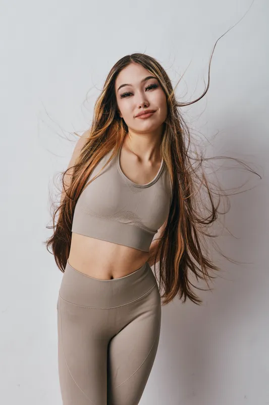 Young woman with long hair in sportswear posing against white wall, active lifestyle, fitness model, confident expression and casual look in studio photo session.