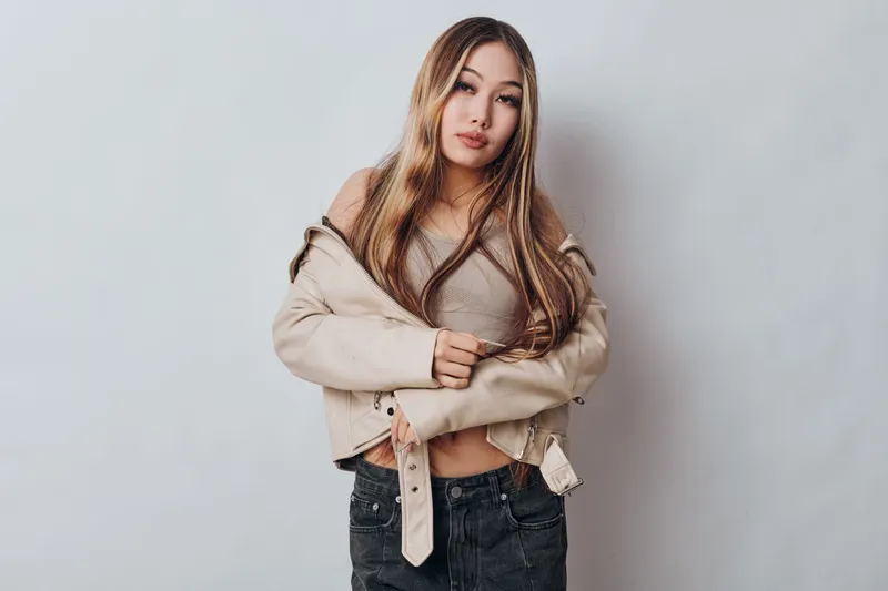 Young woman with long hair wearing casual beige jacket and knitted top posing with crossed arms on plain background for fashion lifestyle and beauty portrait.