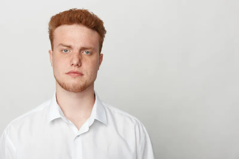 Portrait of a serious young man with red hair and beard wearing a white shirt against a plain light background. Concept of confidence, professionalism, and natural appearance.