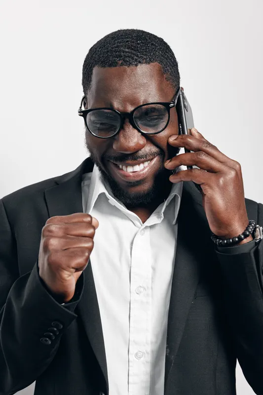 African American man with dark skin wearing glasses and black suit talking on phone and celebrating success with fist pump. Businessman, communication, happiness and achievement concept.