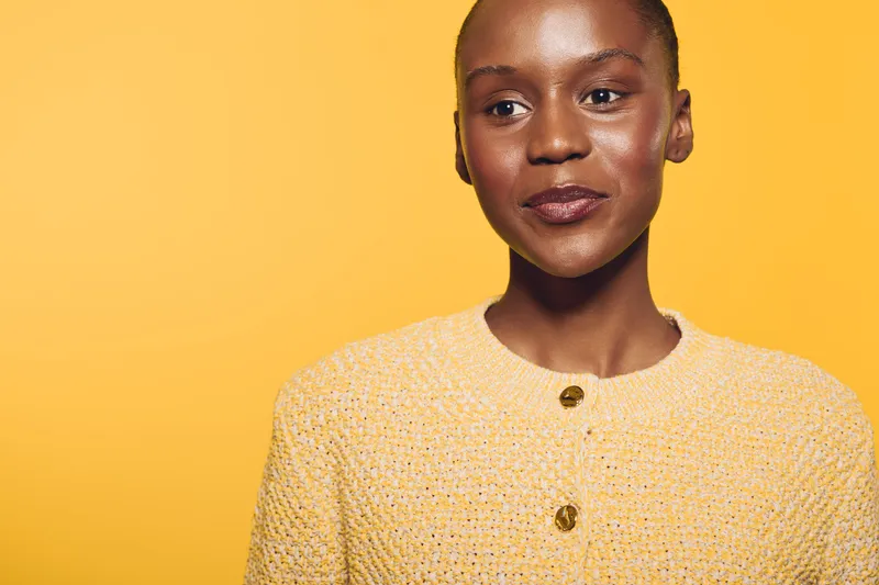 Portrait of a confident dark skinned African woman wearing a yellow sweater against a bright yellow background. Concept of beauty, confidence, fashion, and diversity in studio lighting.