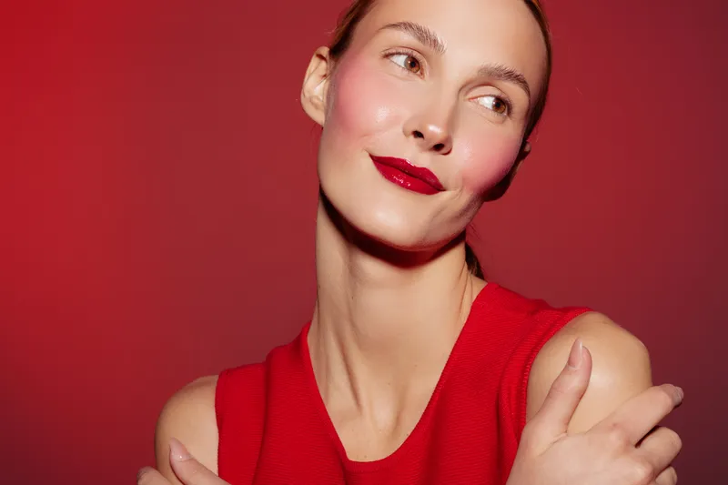 Portrait of a woman with red lipstick and red sleeveless top posing against a red background. Concept of beauty, fashion, makeup, and confident expression.