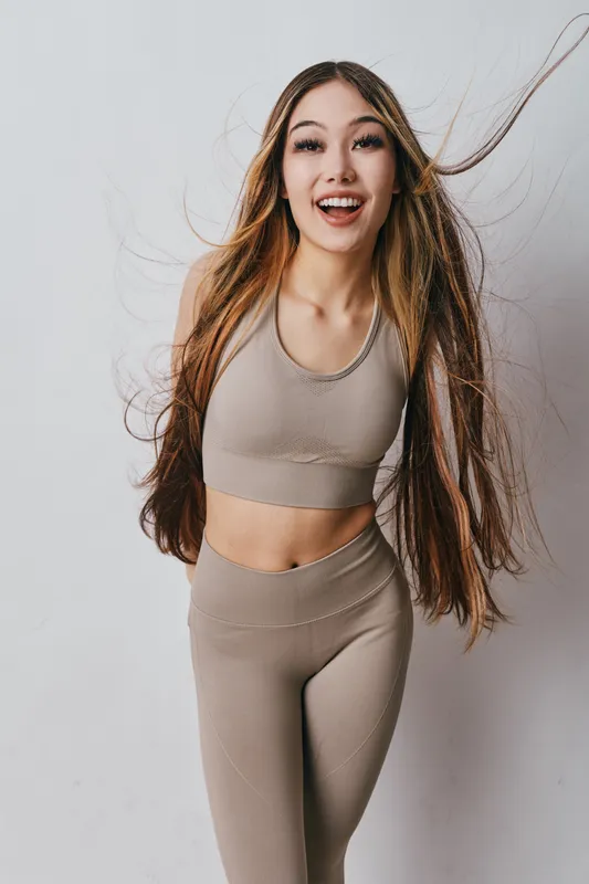 Young woman with long hair wearing beige fitness outfit smiling and posing on white background. Healthy lifestyle, active exercise and wellness concept for workout or sport.