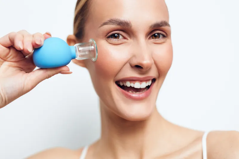 Smiling woman drinking water from blue bottle in close up studio shot on white background for hydration wellness and self care concept Soft light joyful expression