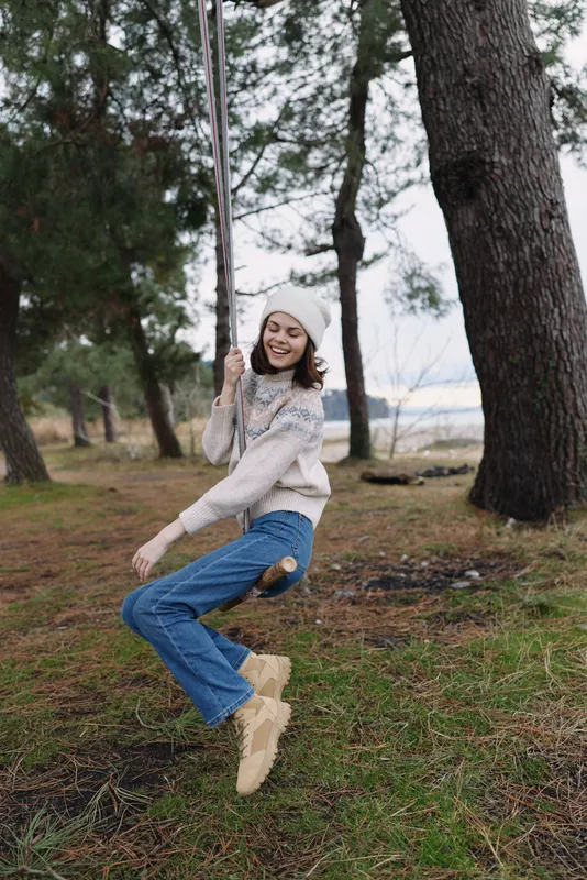 Outdoor swing scene with a smiling girl in a knit sweater and jeans, swinging between trees in a park with soft natural light and a tranquil forest backdrop.