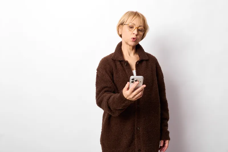 Woman with smartphone, surprise and anxiety in a studio on white background, she studies the screen, concept of communication and technology, mobile updates