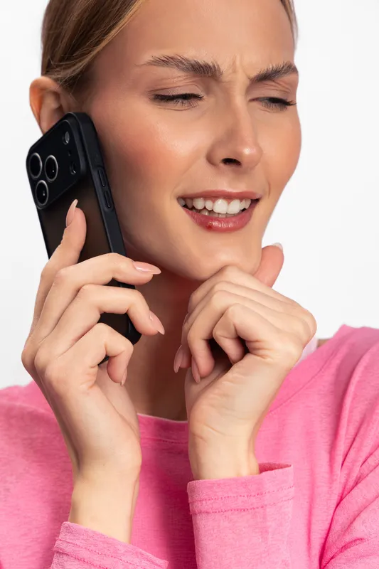 Young woman in pink shirt talks on smartphone with eyes closed and thoughtful expression. Isolated on white background. Concept of communication, technology, and emotion.