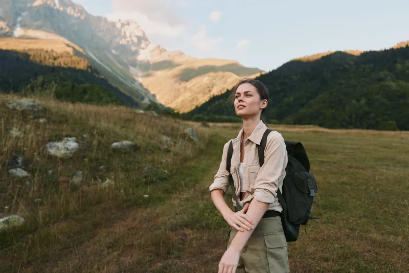 Woman hiker backpacking through alpine meadow gazing toward distant peaks, enjoying outdoor lifestyle in rugged landscape