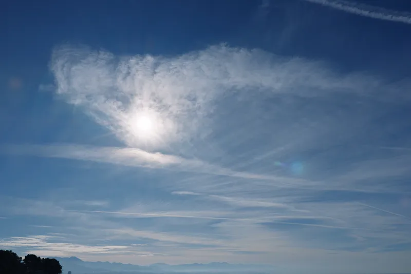Clear blue sky with bright sun and wispy clouds over a distant horizon, serene expansive daylight atmosphere for nature, landscape and travel themed visuals