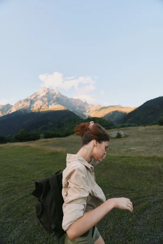 Woman hiking in an alpine meadow with a backpack, mountain backdrop, and clear blue sky, showcasing outdoor lifestyle, adventure, wellness, and fresh air, and inspiration.