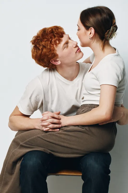 Couple sitting with woman on man lap looking at each other intimately in casual clothes isolated on white background for love, relationship and affection concept.