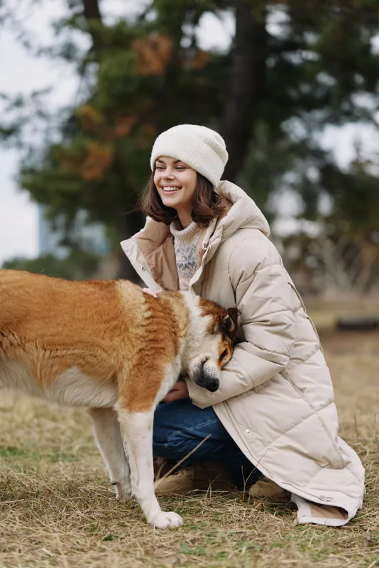 Woman, dog, outdoor, coat, winter, affection, kneeling, cuddling, pet, friend in a field sharing a gentle moment beside a warm coat on a chilly day.