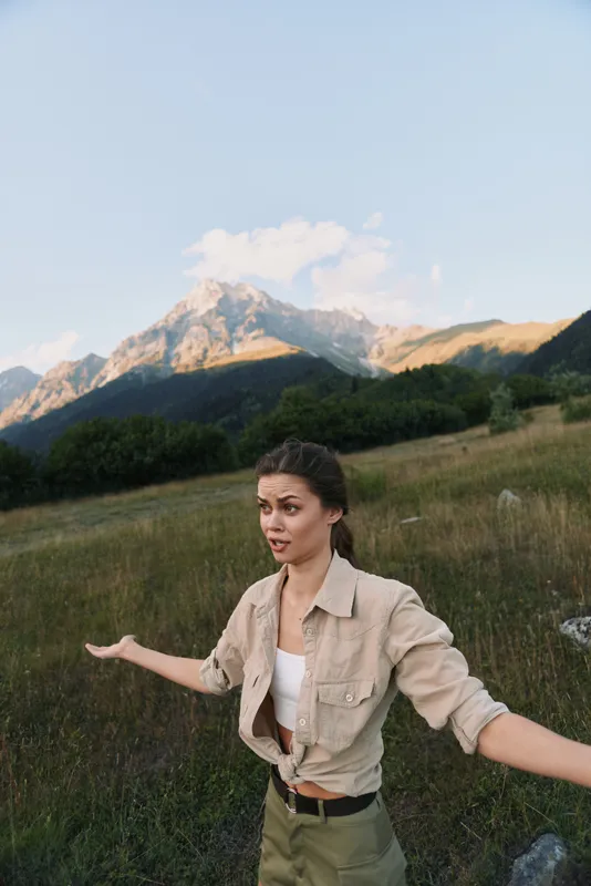 Young woman with brunette hair stands in a mountain meadow with arms outstretched expressing freedom and connection to nature during a clear day.