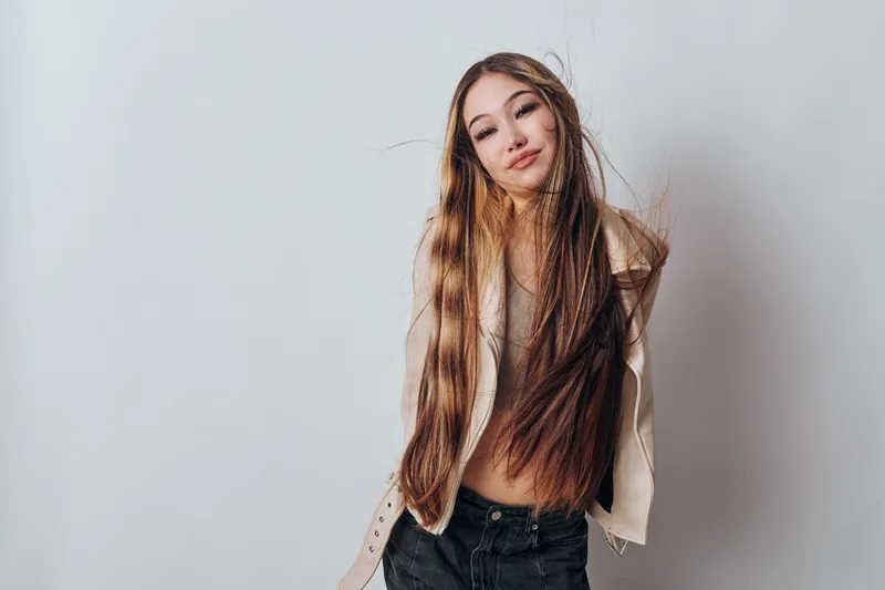 Young woman with long hair and casual jacket posing with smile against neutral background. Fashion, beauty, hair care and youth style concept with confident female portrait.