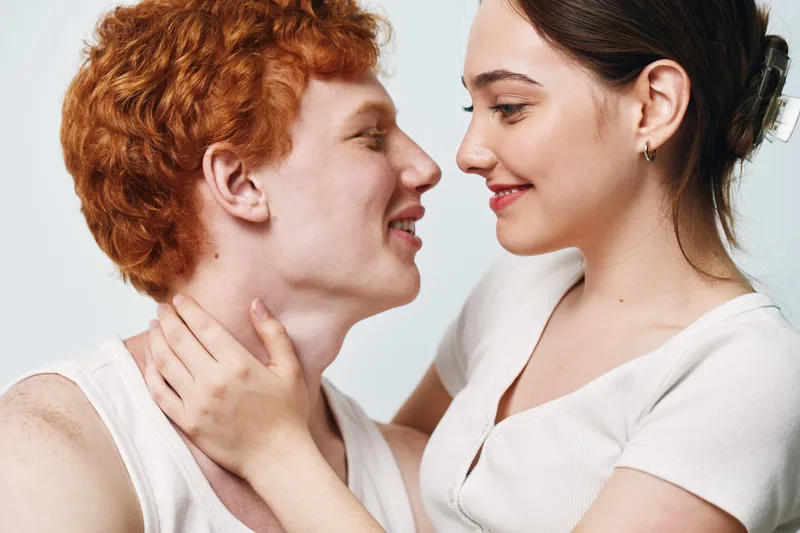 Couple, love, affection and romantic moment with woman and man close, smiling and looking each other with happiness and intimacy in studio on plain background.