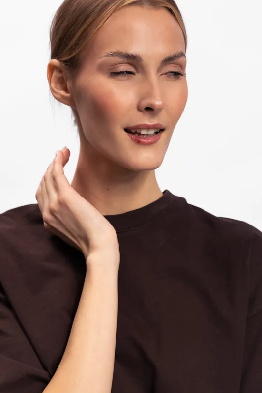 Young woman with closed eyes and subtle smile touches her neck gently. She wears a dark top against a plain white background. Concept of calm, beauty, and natural expression.