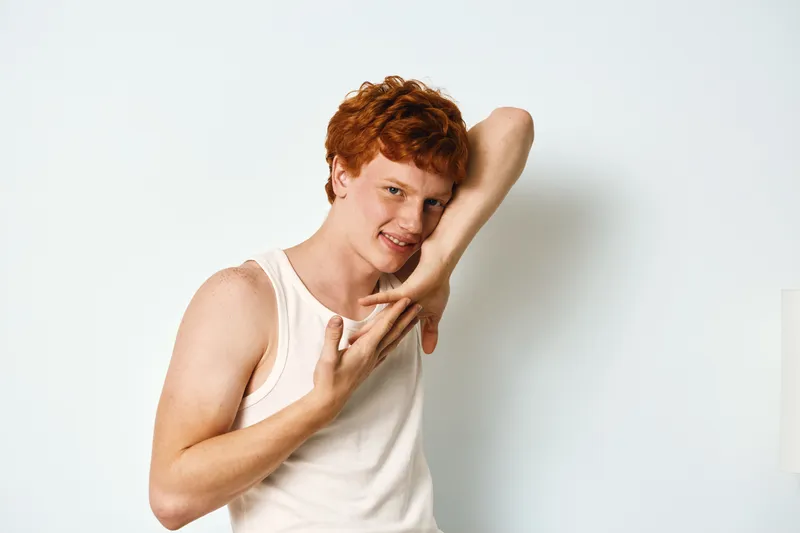 Young man with red hair, smile and casual sleeveless shirt posing with hand gesture in front of white background. Portrait, studio, isolated, positive and natural expression.