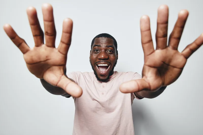 African man with dark skin smiling and reaching hands forward in casual shirt on white background for happiness and positive emotion concept.