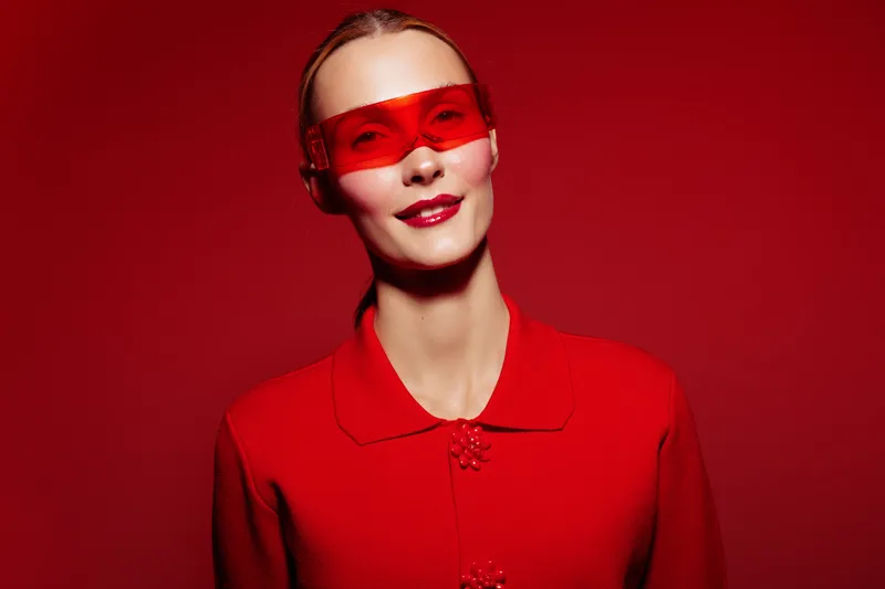 Portrait of a smiling woman wearing red sunglasses and a red sweater against a red background. Concept of fashion, style, confidence, and modern accessories in studio lighting.