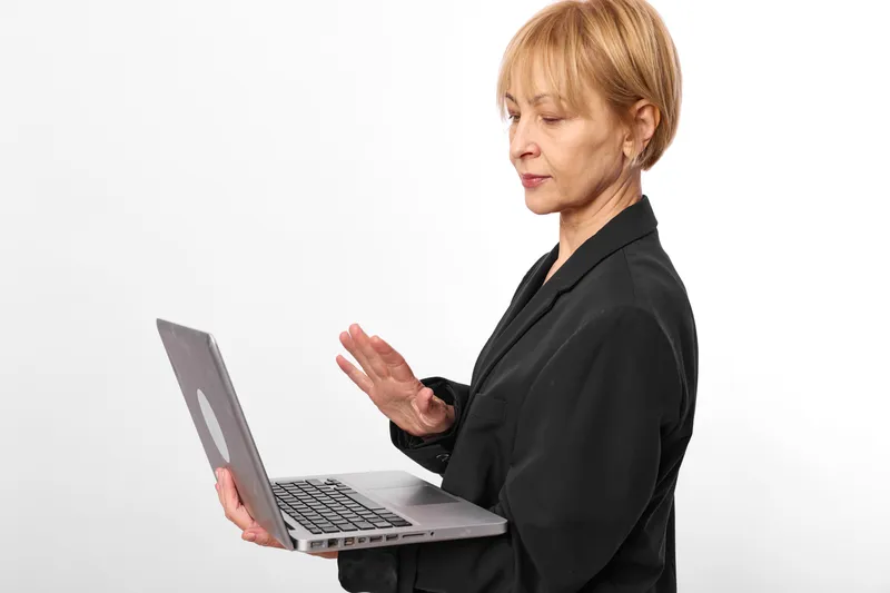 Stressed woman with laptop in business attire gestures during remote communication. Side view on white background suggests high anxiety meeting call at work stress.