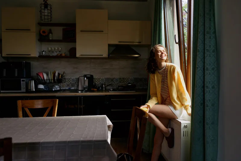 Woman relaxing by a sunny kitchen window, casual home lifestyle scene with cozy light and candid mood.