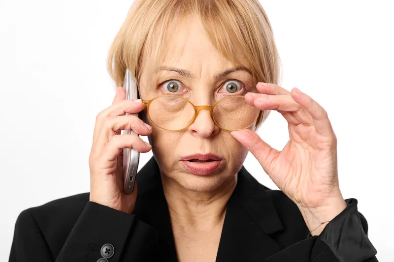 Woman applying eye patch during a phone call in a studio close up portrait. Skincare beauty selfcare and anti aging concept, calm focused expression, soft light on white background.