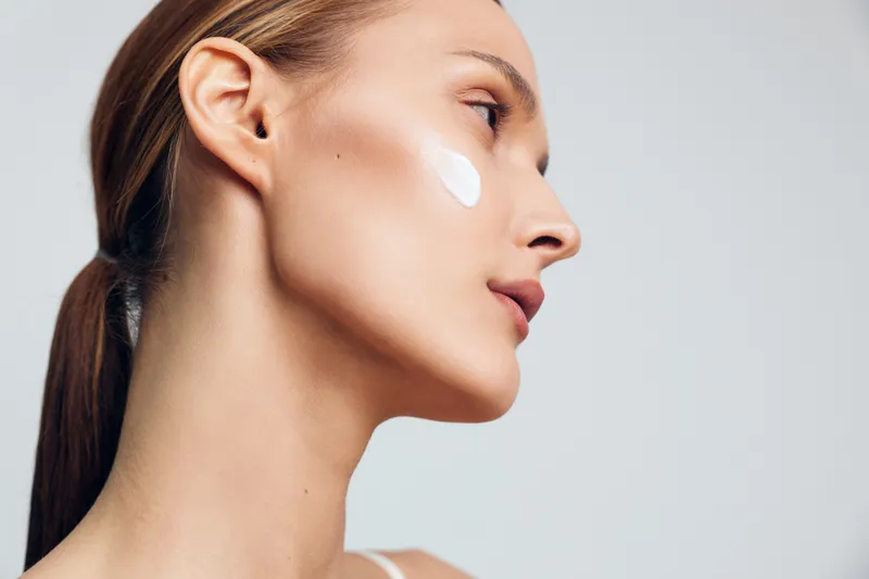 Close up profile of a woman with white cream on her cheek, showcasing skincare routine, smooth skin, and a healthy glow in a minimalist portrait.