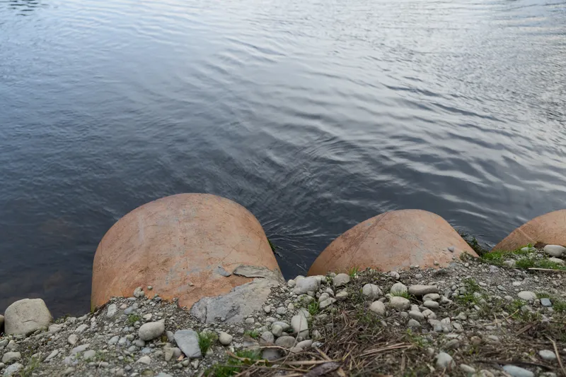 Calm lake water touches a rocky shoreline with rounded boulders and small pebbles, no people, peaceful outdoor lifestyle, natural landscape texture, soft daylight, blue tones, serenity