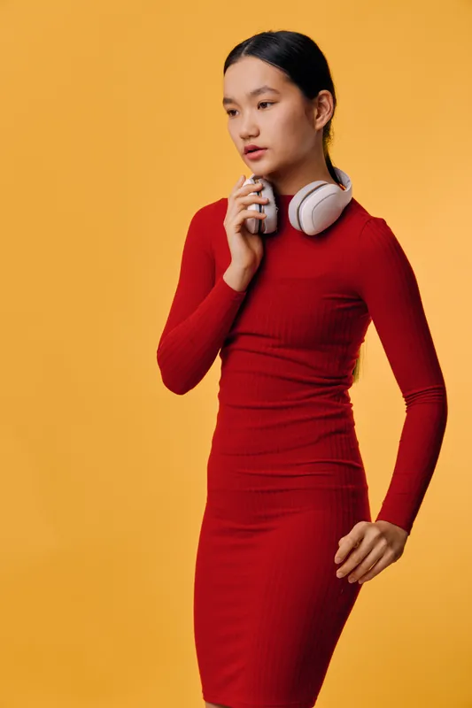 Young woman in red dress holding headphones and smartphone on yellow background. Fashion, technology, lifestyle and communication with casual look and studio lighting portrait.
