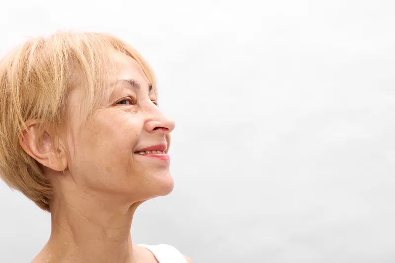Woman portrait mature blonde profile smile closeup headshot shoulders, senior elderly female, calm gentle expression, soft light on white background, studio, copy space