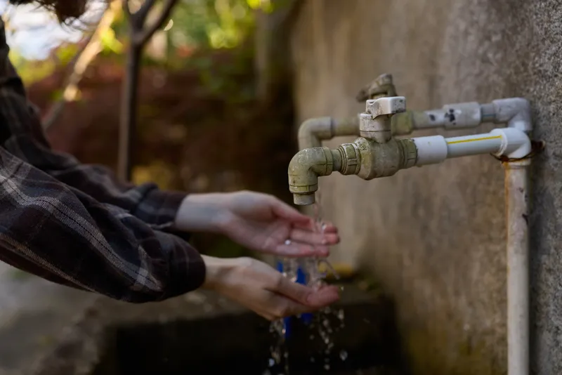 Woman washing hands at an outdoor faucet, water droplets spraying, casual attire, lifestyle moment emphasizing hygiene, cleanliness and everyday wellness