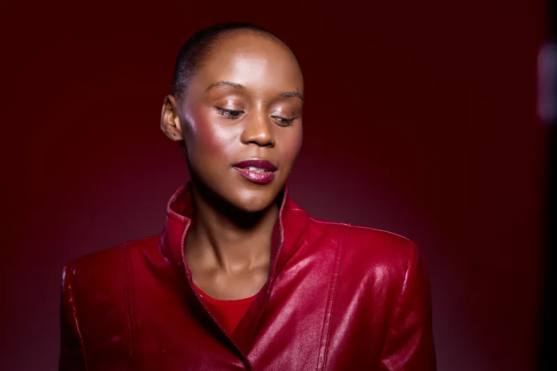 Portrait of a confident black woman with dark skin wearing a shiny red leather jacket against a deep red background. Concept for fashion, elegance, and beauty with strong color contrast.