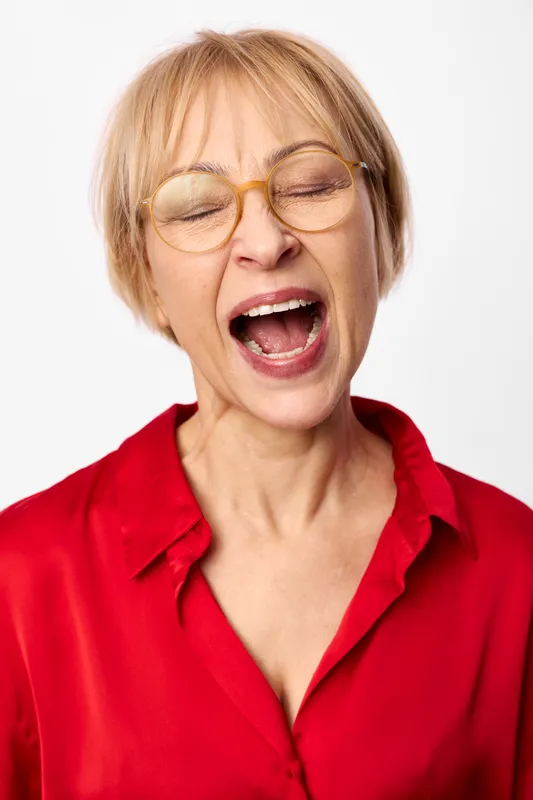 Senior woman yawning in a red shirt, eyes closed and mouth open, closeup portrait on plain white background, expression shows fatigue and tiredness, concept for stress burnout and mental health
