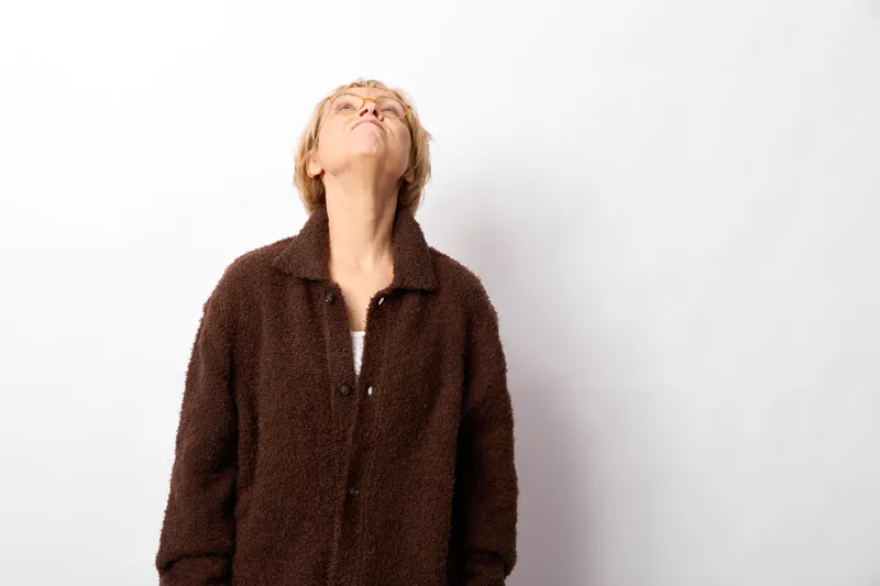 Woman coat portrait looking upward eyes closed studio white background soft light calm expression winter fashion minimal composition